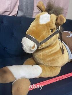 Cheval de peluche géant avec selle assis sur un coussin en peluche animal brun